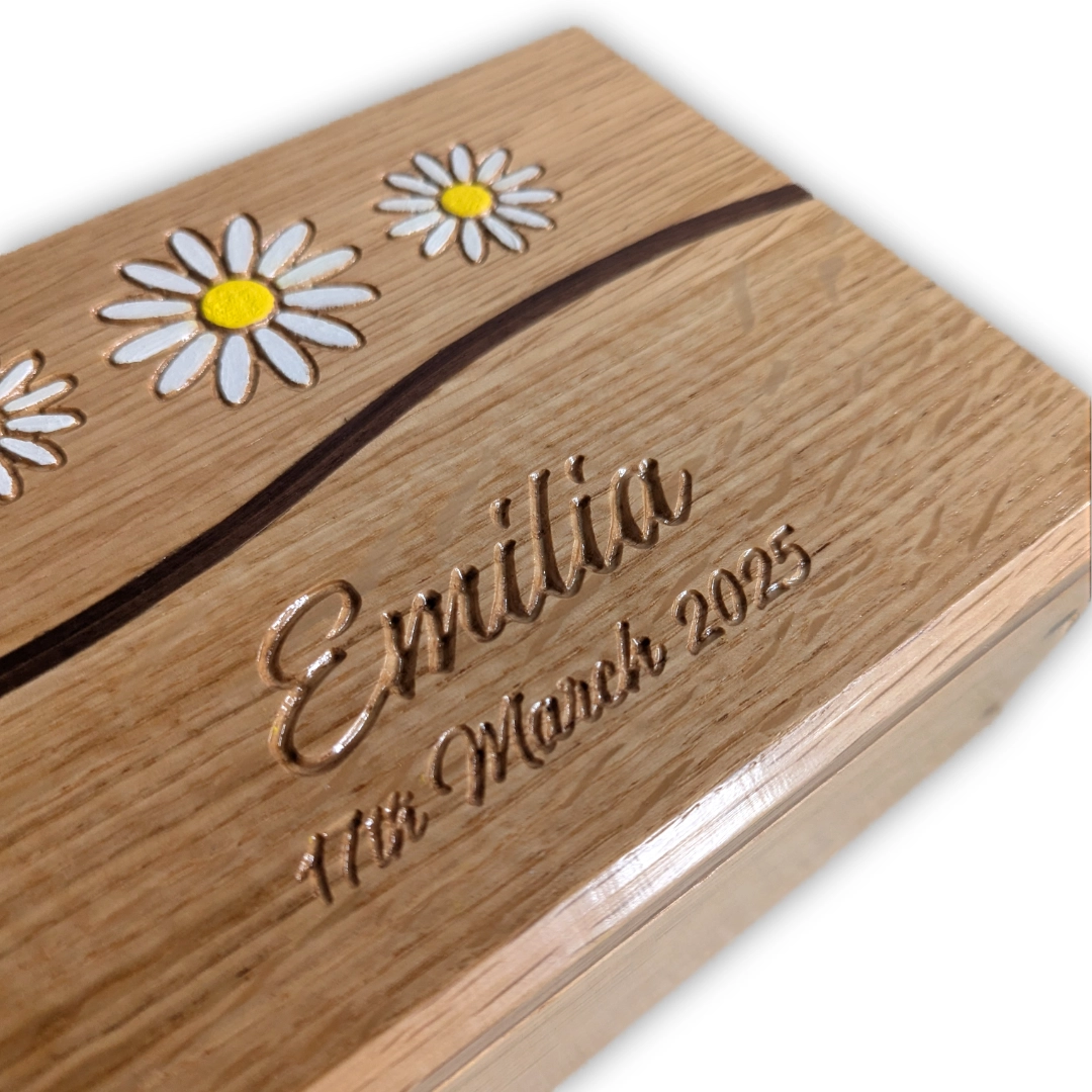 A wooden box engraved with a name and birthday and decorated with carved, painted daisies.