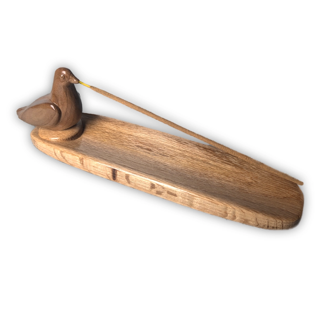 A wooden bird on a tray with an incense stick held in a hole in its beak.