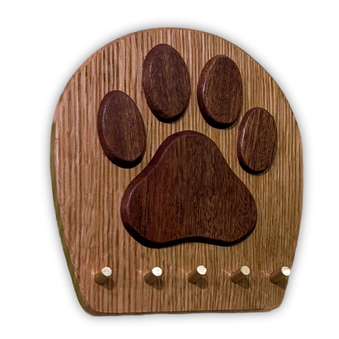 A round plaque with a pawprint in darker wood, with five brass pegs.