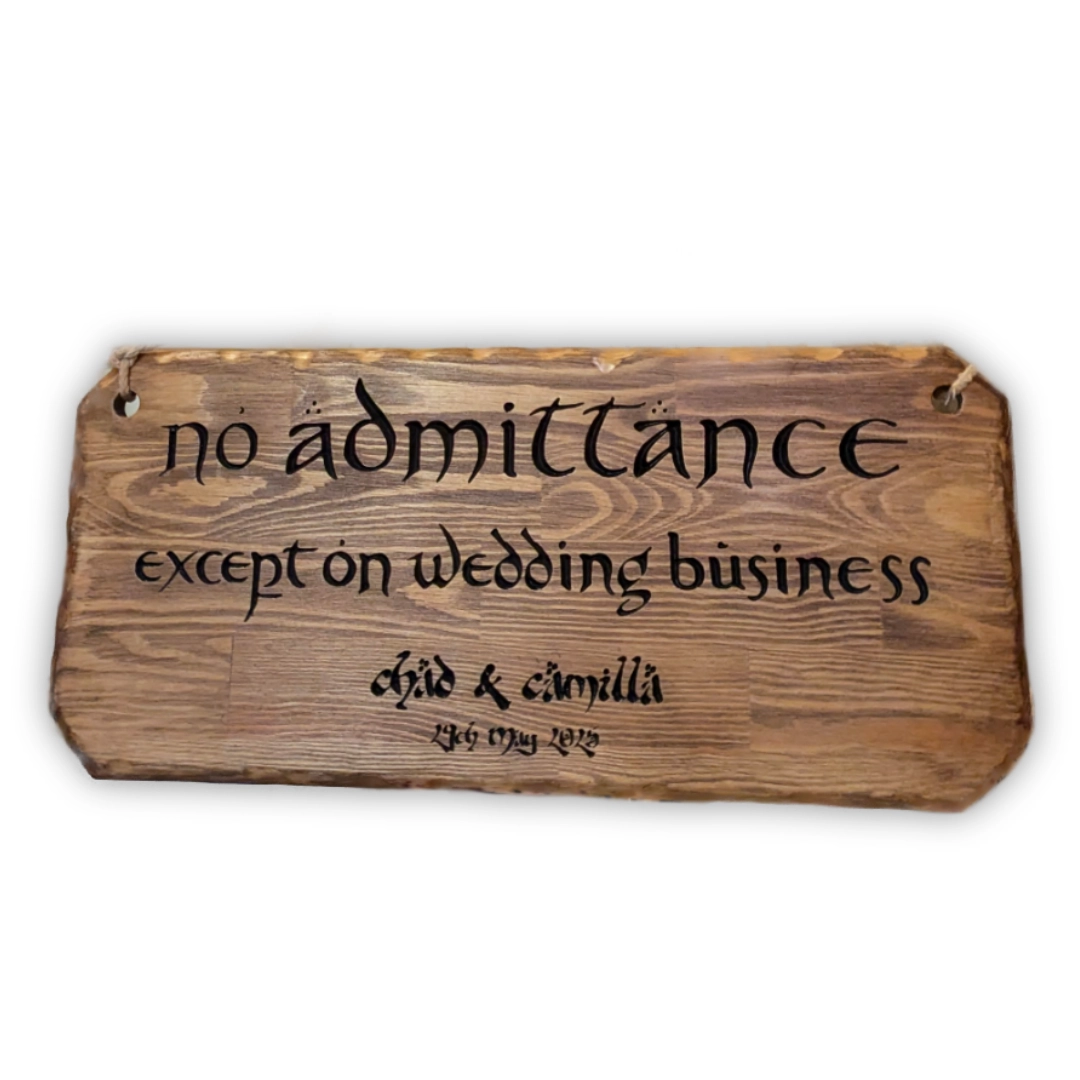 A rough-hewn noticeboard engraved with 'No admittance except on wedding business' along with the couple's name and wedding date, in a Tolkien-esque font